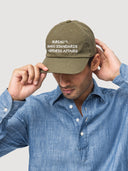 Menswear model shot side view wearing a olive green mango cap with text embroidery, wearing a blue chambray shirt on a light grey background
