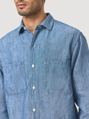 Close-up pocket view of a blue denim chambray worker shirt worn by a model on a light gray background