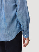 Close-up sleeve shot of model wearing a Coconut Residence chambray blue denim shirt with a neutral background. Yellow tack stitch on sleeve placket.