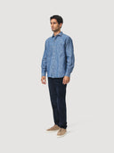 Side front view of model wearing a blue Coconut Residence chambray shirt and dark blue corduroy trousers on a white background.