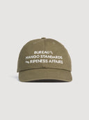 Front view or Coconut Residence olive green mango cap with white text embroidery on a light grey background